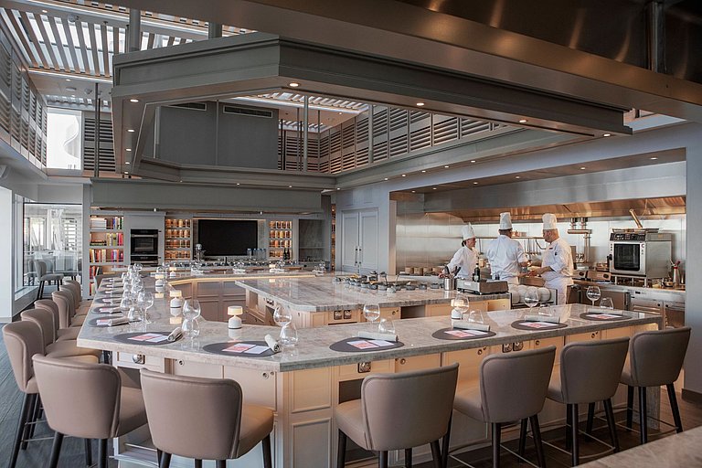 Modernes Restaurant auf einem Kreuzfahrtschiff, mit einer U-Tafel und Liveköchen. 